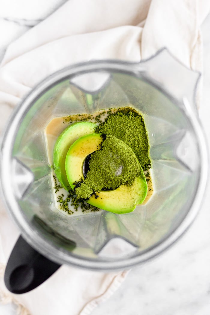 A blender filled with nut milk, avocados, maple syrup, vanilla extract, matcha, and salt.