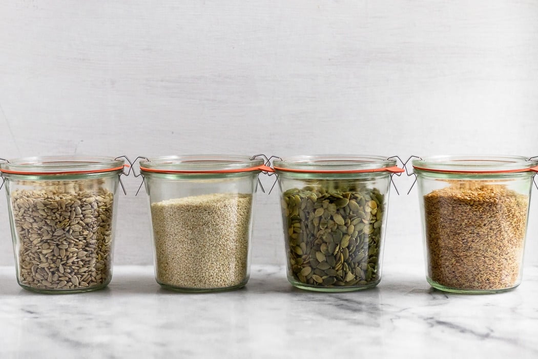 Line of 4 large jars each filled with different seeds for seed cycling.