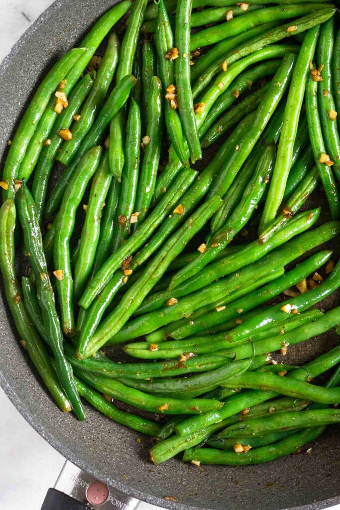 Sautéed green beans with garlic in a large skillet.