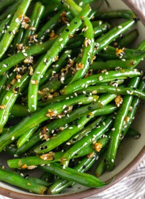 Sesame green beans with garlic in a large white bowl.