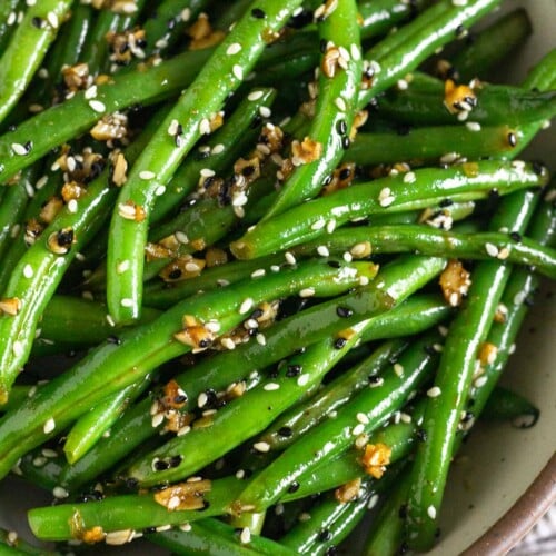 Sesame green beans with garlic in a large white bowl.