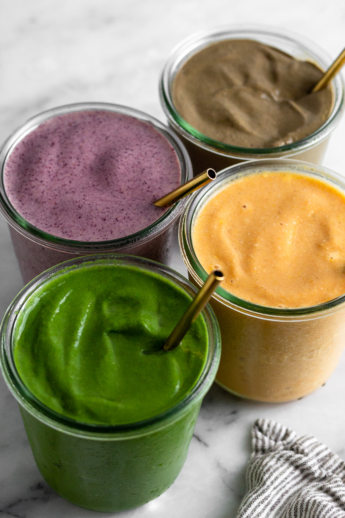 Four different flavors of smoothies in 4 different jars with straws in them.