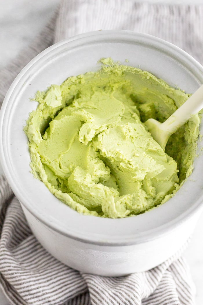 Avocado frozen yogurt in an ice cream maker bowl with a spatula sticking out of it.