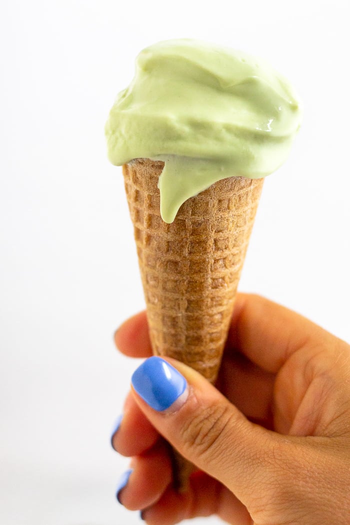 A hand holding a sugar cone filled with avocado frozen yogurt.