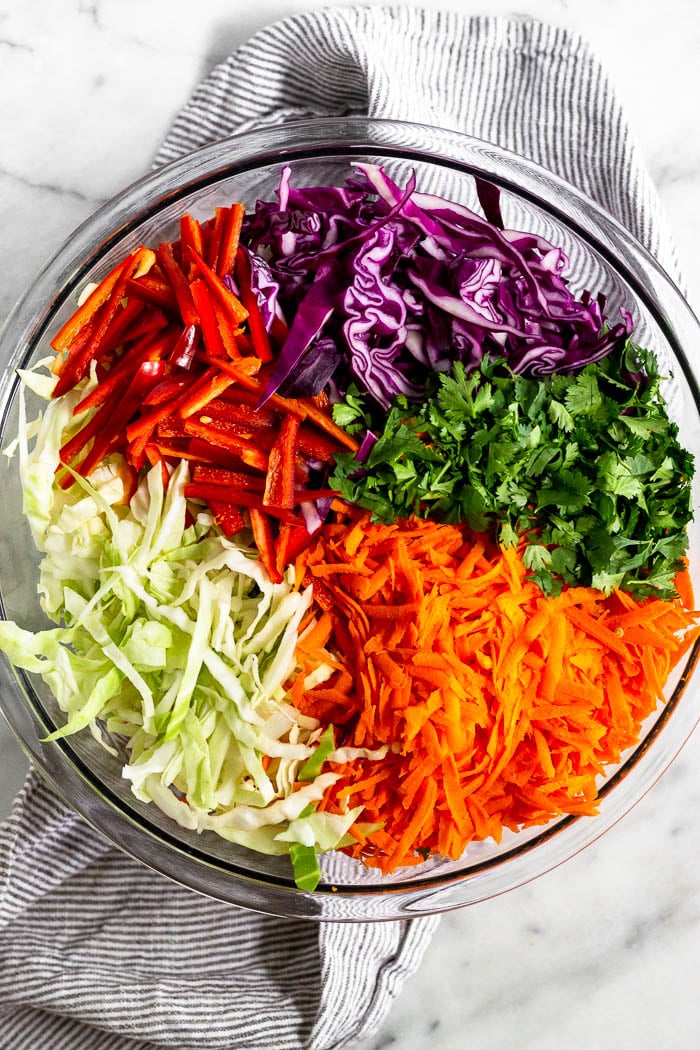 Large glass bowl filled with shredded cabbage, cilantro, shredded carrots, and sliced red pepper.