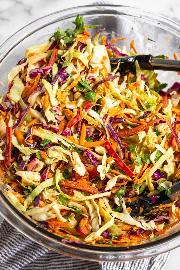 A bowl of Mexican coleslaw with tongs resting in it.