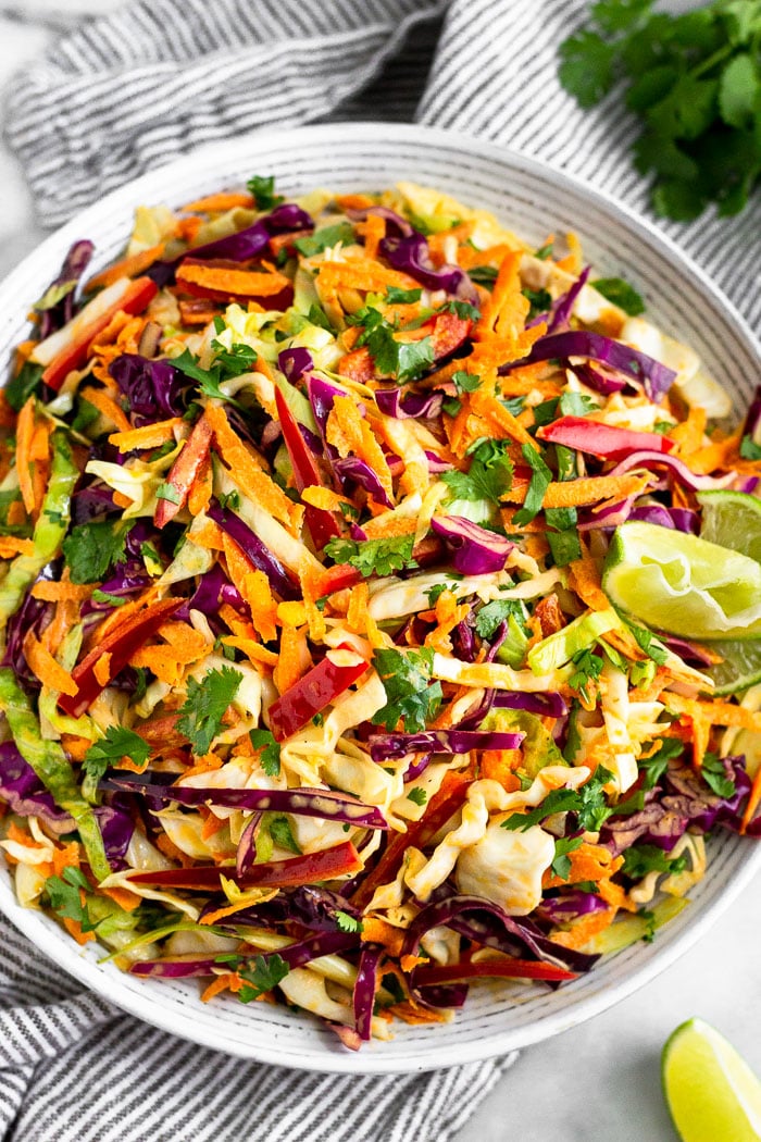 Large bowl of chipotle Mexican coleslaw garnished with lime wedges and surrounded by cilantro and another lime wedge.