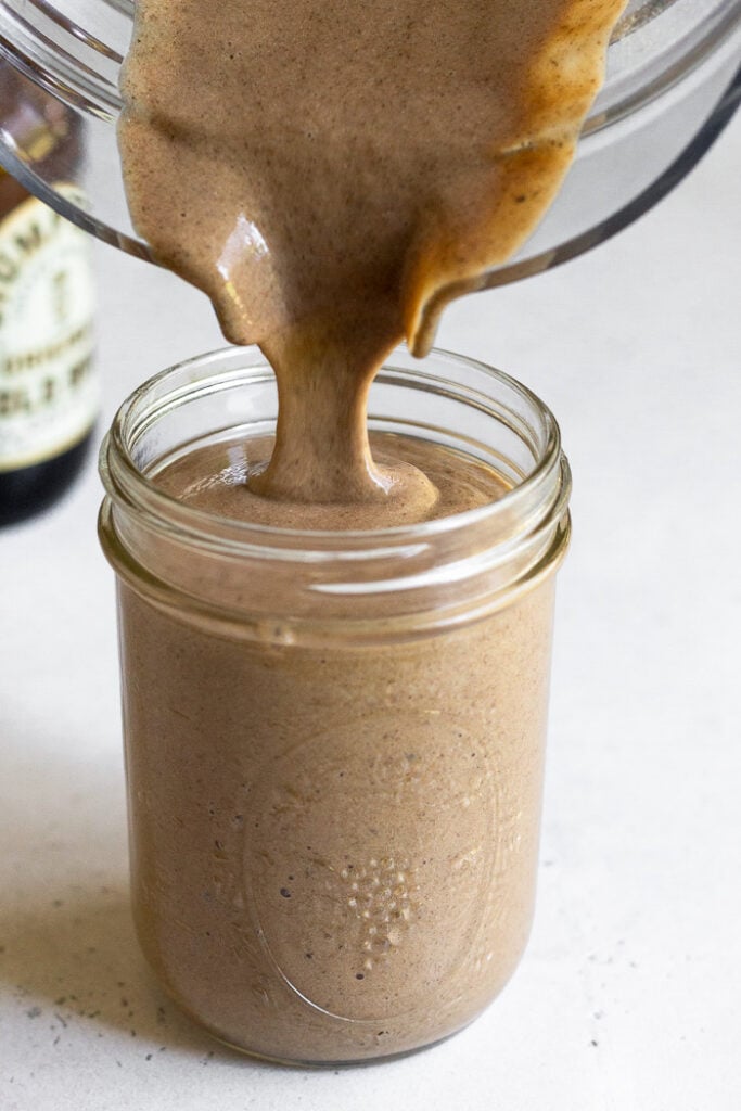 Protein coffee smoothie being poured into a glass jar. Behind it is a bottle of cold brew coffee.