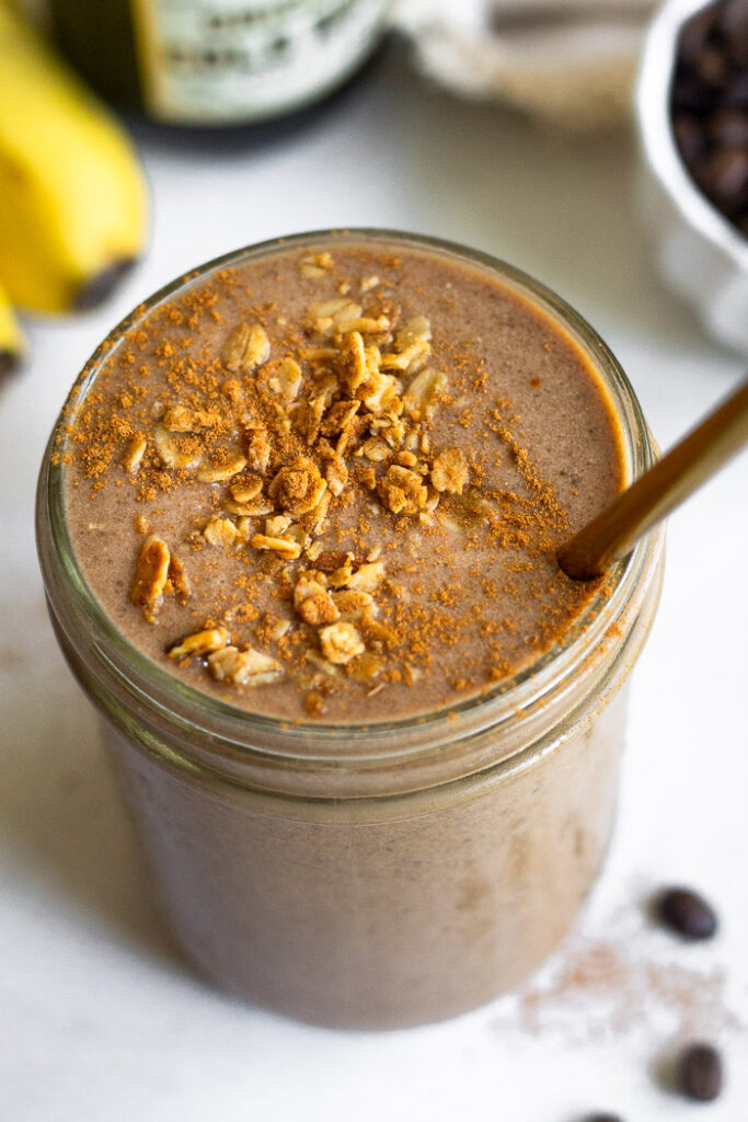 Protein coffee shake in a jar topped with granola and cinnamon with a straw in it.