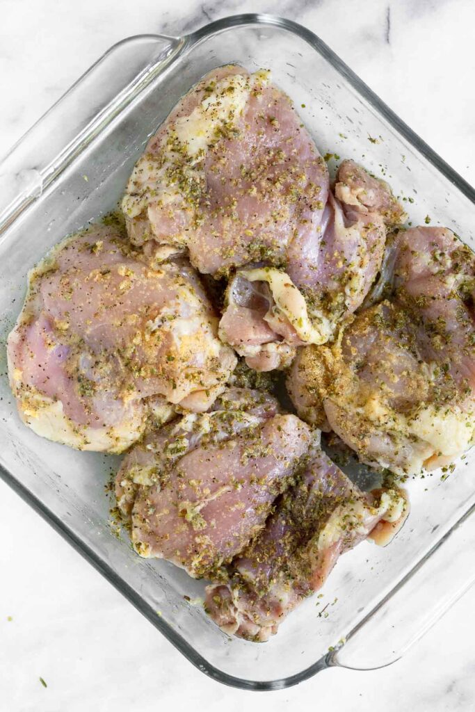Overhead shot of chicken thighs in a baking dish coated with oil, lemon, and spices.