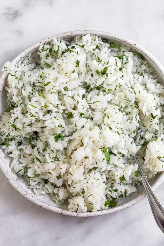 Bowl of white rice mixed with fresh herbs. A spoon is in the bowl.