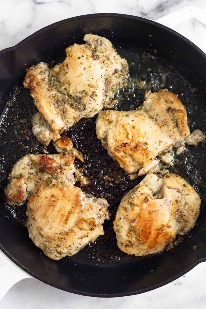 Cast iron with four seasoned and cooked chicken thighs in it.