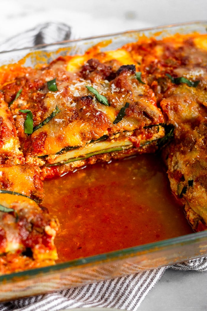 Low carb zucchini lasagna in a pan with a slice taken out of it. It is garnished with parmesan cheese and fresh basil.