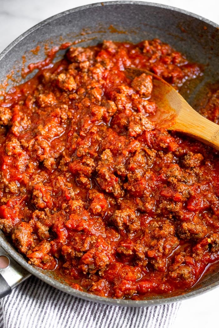 A large saute pan filled with cooked ground beef mixed with pasta sauce.