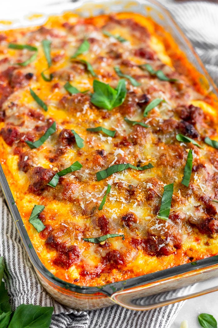 Large glass baking dish filled with zucchini lasagna garnished with fresh basil and parmesan cheese. The pan is sitting on a blue stripped towel.