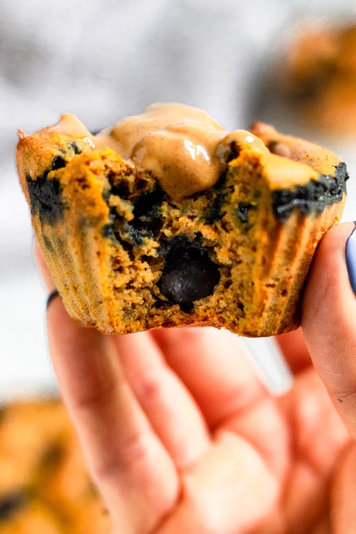 Hand holding up a sweet potato blueberry protein muffin with a bite taken out of it topped with peanut butter.