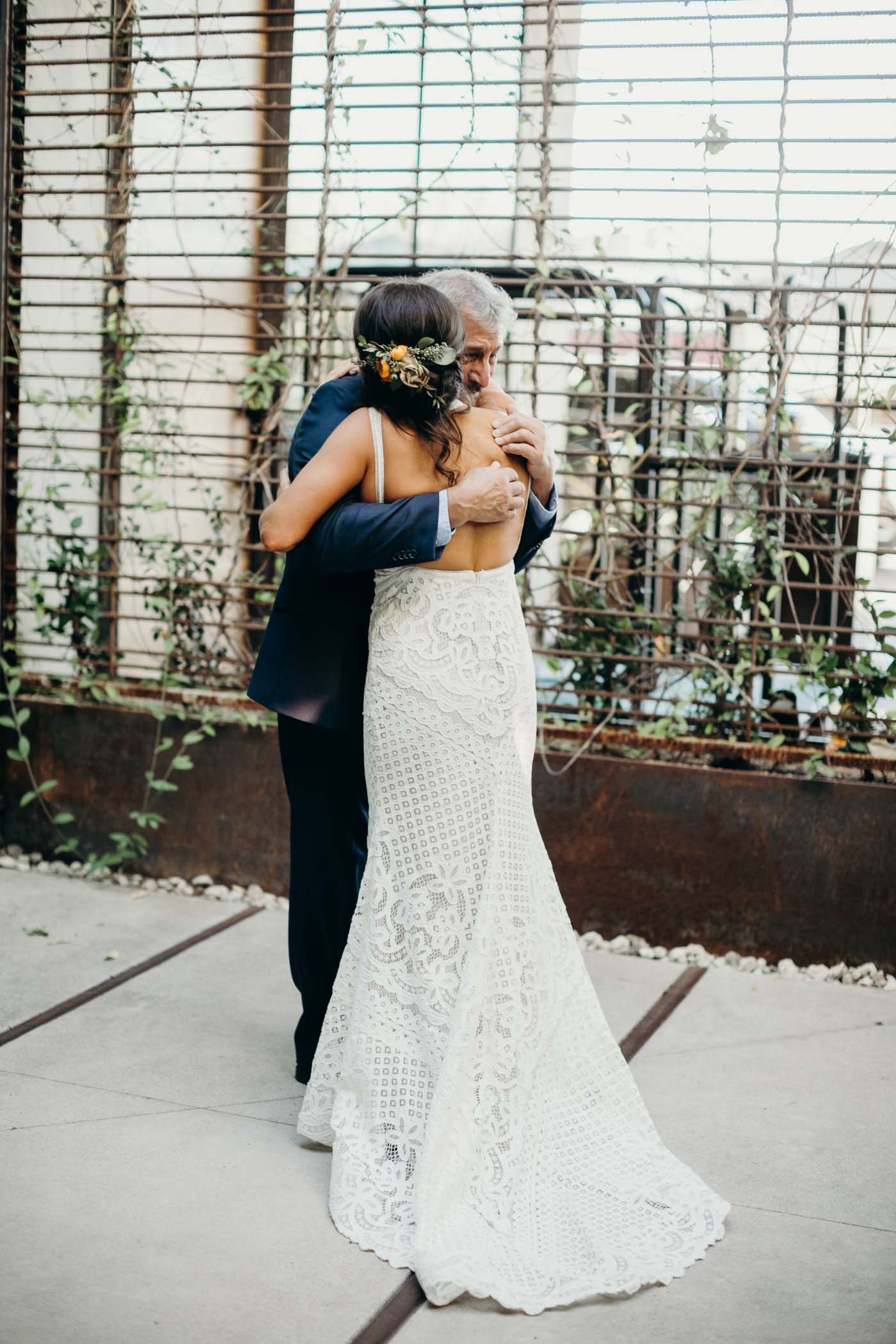 Bride hugging her dad on her wedding day. You can see the back of her and she is wearing an open back lace boho dress.