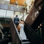 Bride and a groom walking up the stairs after their first look with the bride's father looking down at them from above.