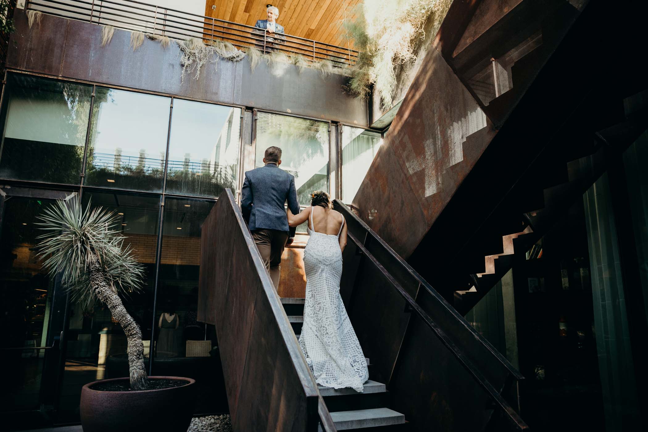 Bride and a groom walking up the stairs after their first look with the bride's father looking down at them from above.