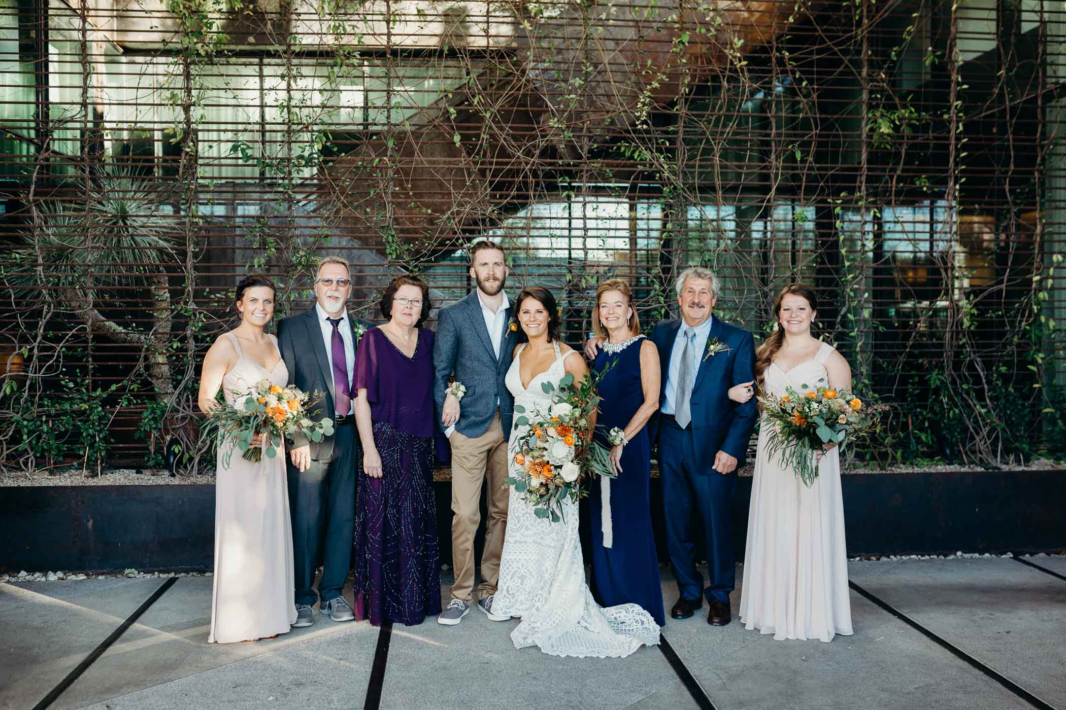 Bride and groom with with family members on both sides of them. the bride is holding a large bouquet and has on a boho dress.