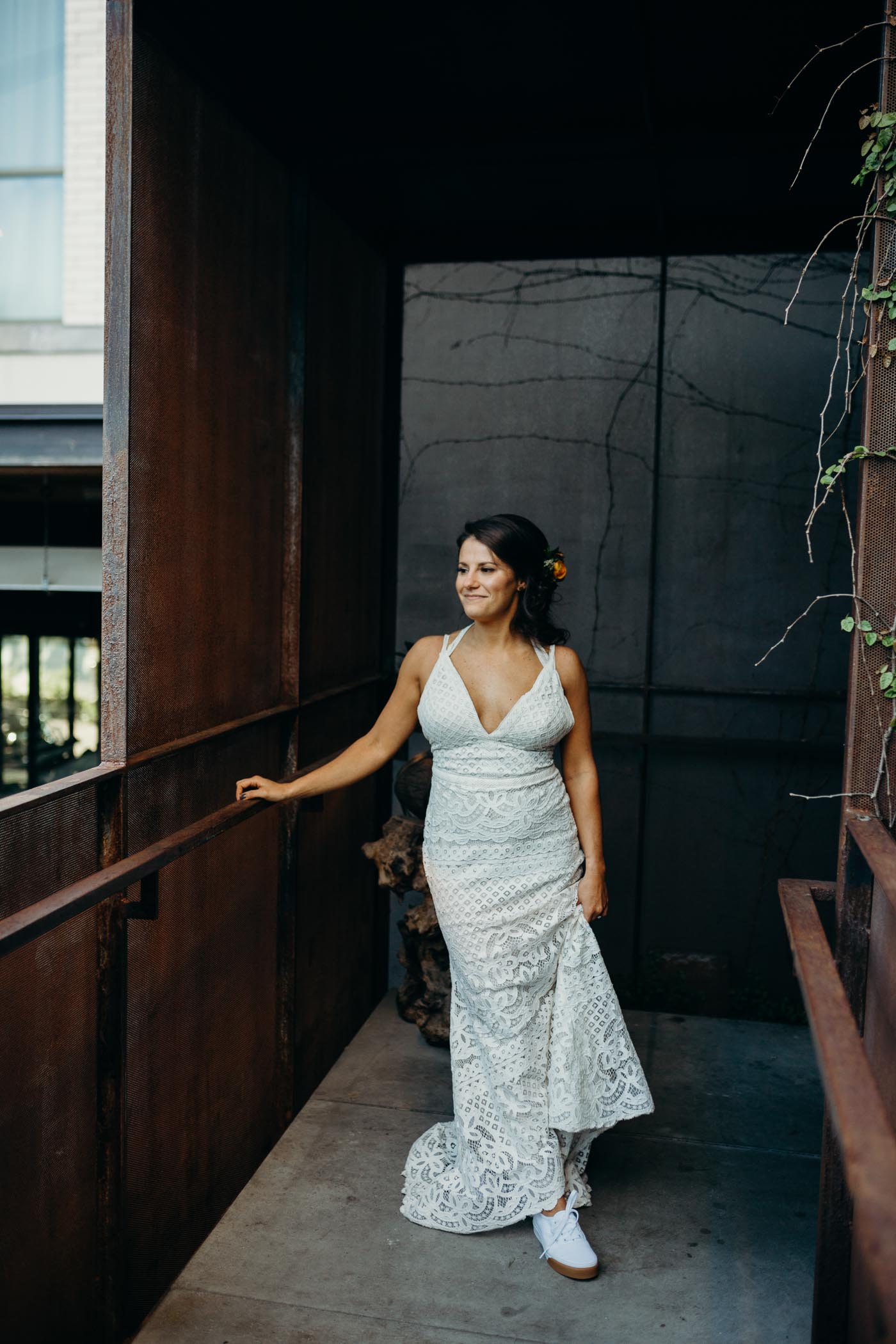Girl in a lace boho wedding dress holding up one side of it. She is wearing vans.