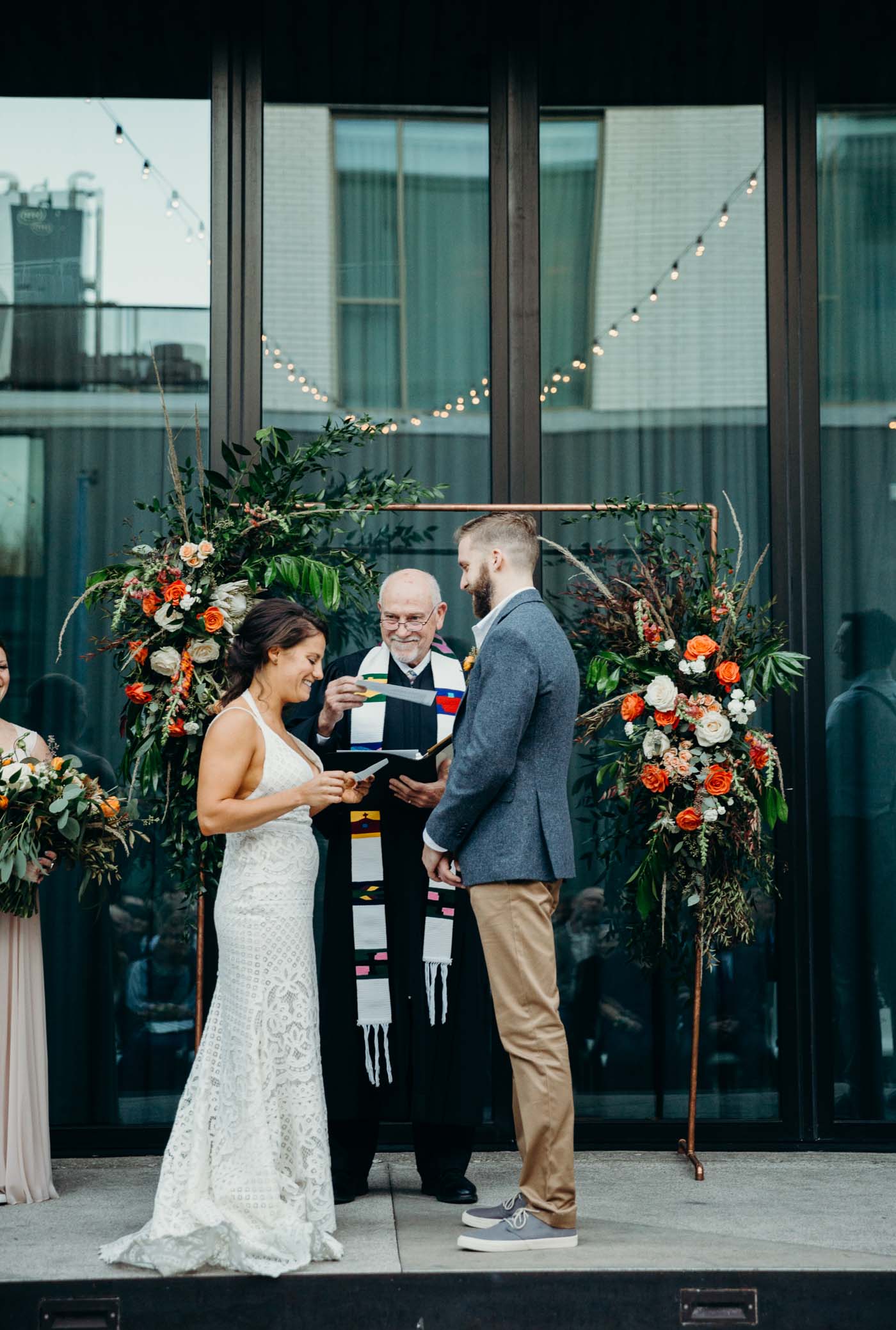 Bride reading her vows to her fiancé at the alter on their wedding day. Behind them is an arch covered with flowers. It is a boho wedding.