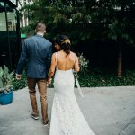 The back of a bride wearing a boho lace wedding dress. She is walking with her husband just after they got married.