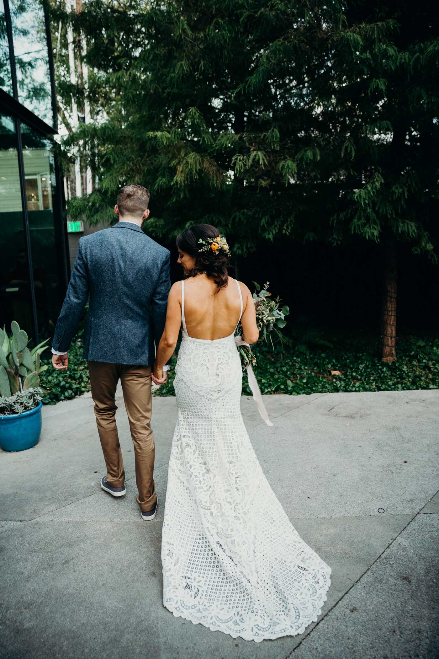 The back of a bride wearing a boho lace wedding dress. She is walking with her husband just after they got married.