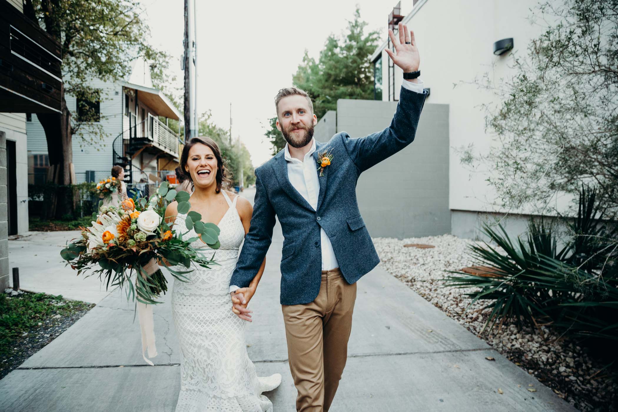Bride and groom cheering after they just got married. They are holding hands. The groom has the other hand raised in the air the the bride is holding her bouquet.