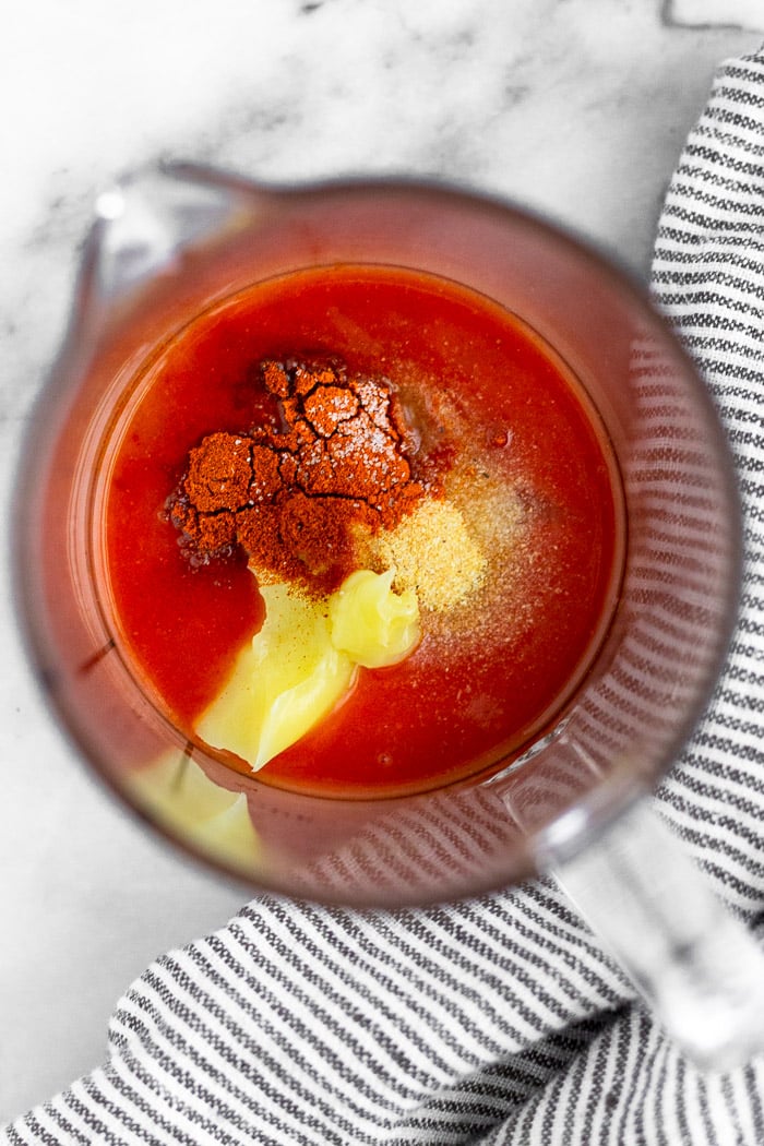 Glass mixing jar filled with hot sauce, ghee, lemon juice, garlic powder, paprika, cayenne, and salt and pepper.