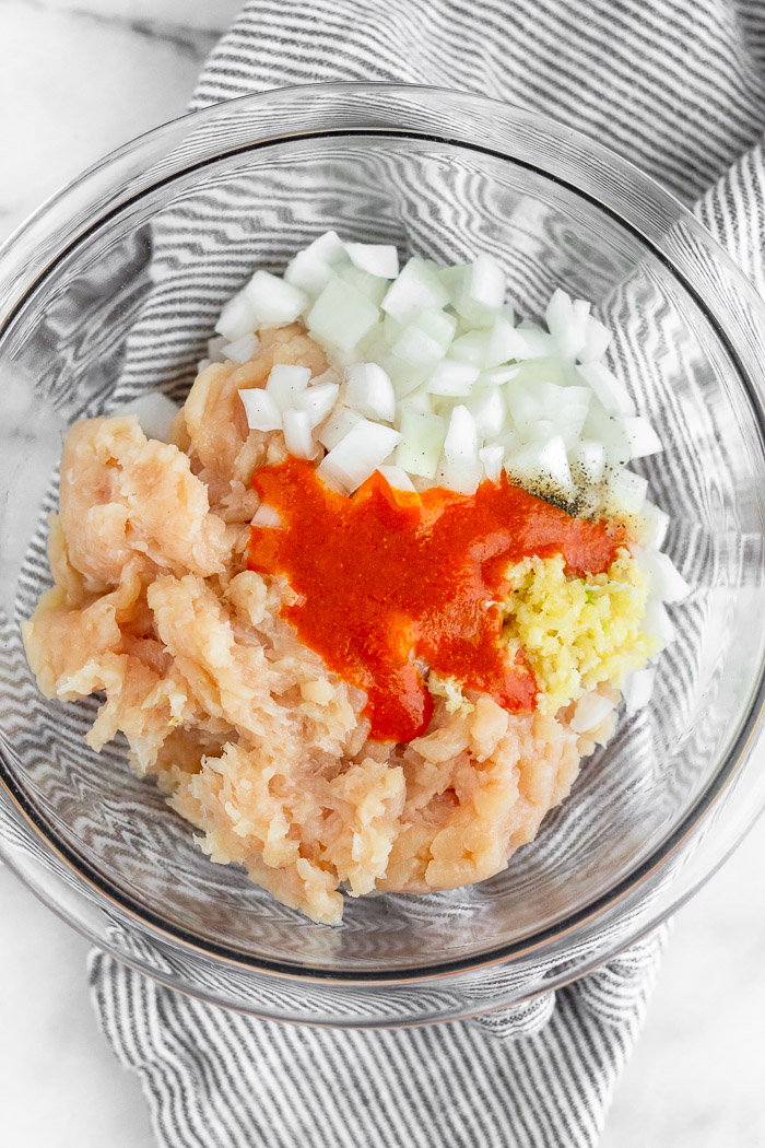Bowl of ground chicken, chopped onion, minced garlic, and buffalo sauce.