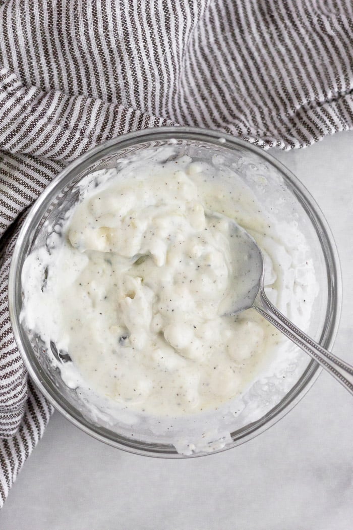 Bowl of homemade healthy blue cheese dressing with a spoon in it. It is next to a kitchen towel.