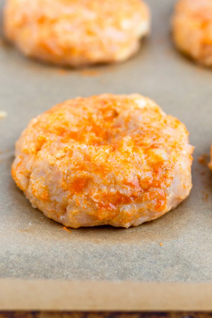 Raw chicken burgers on a baking sheet.