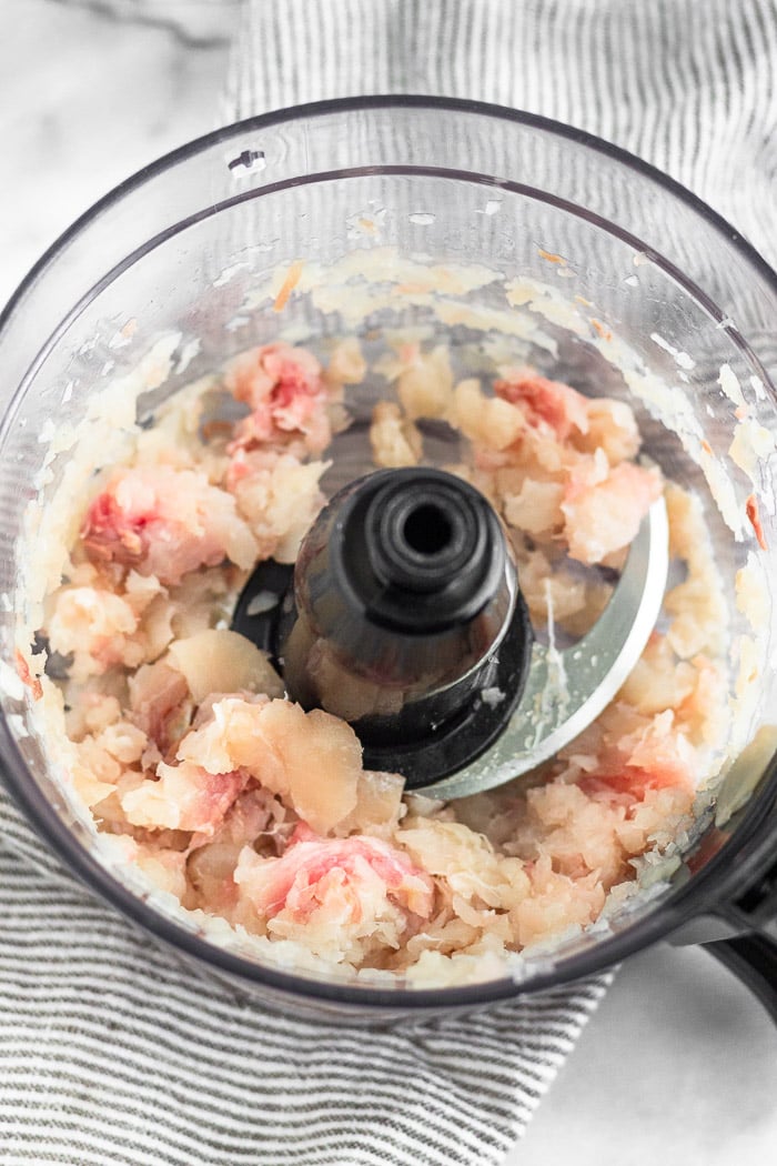 Raw Mahi Mahi in a food processor that has been broken down into small pieces.