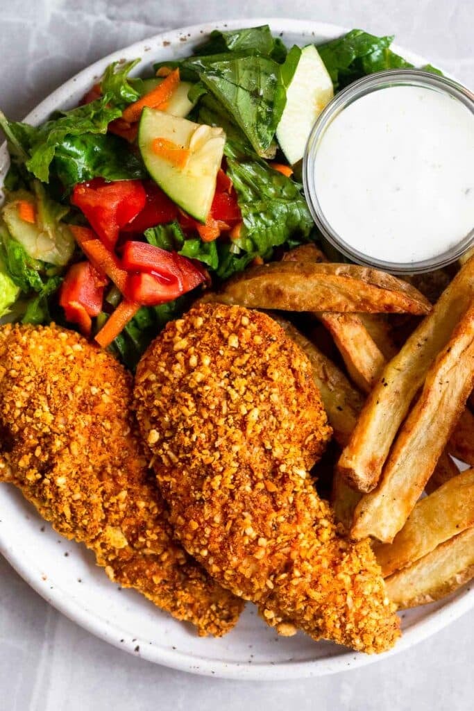 Overhead shot of a plate of baked buffalo chicken tenders with a salad, side of dressing, and french fries.