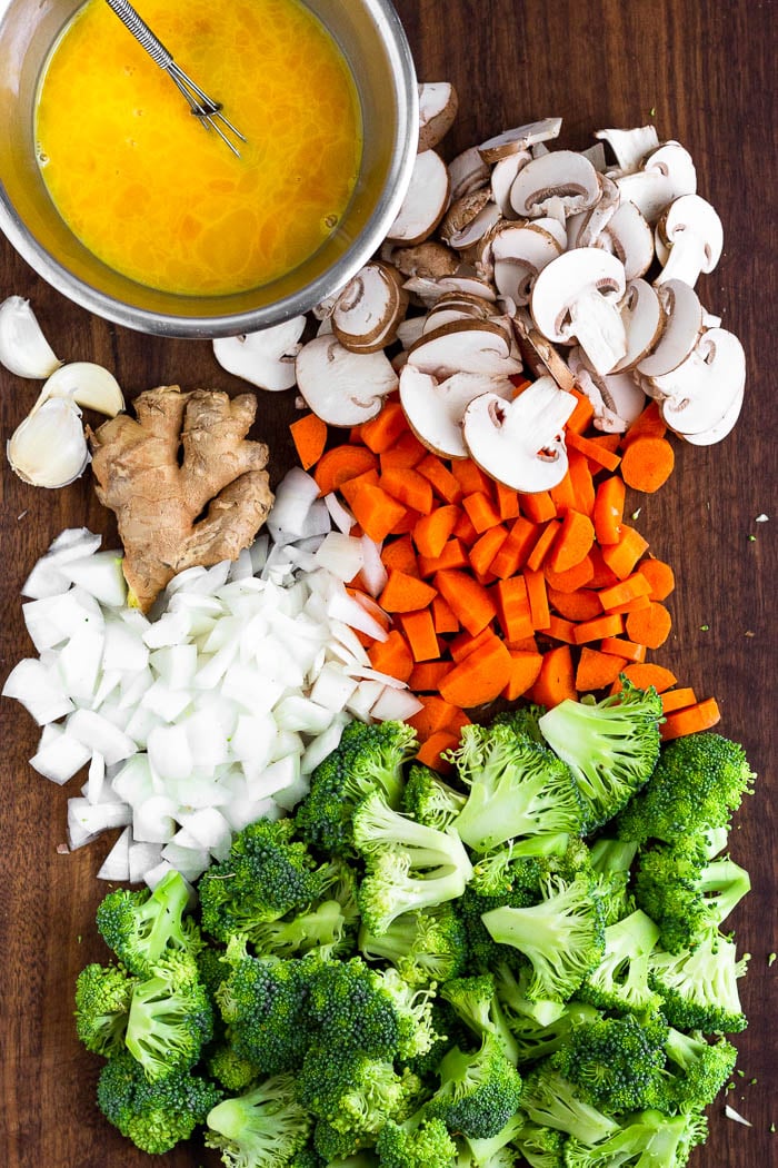 Cutting board filled with chopped broccoli, onions, carrots, mushrooms, and a bowl of whisked eggs.