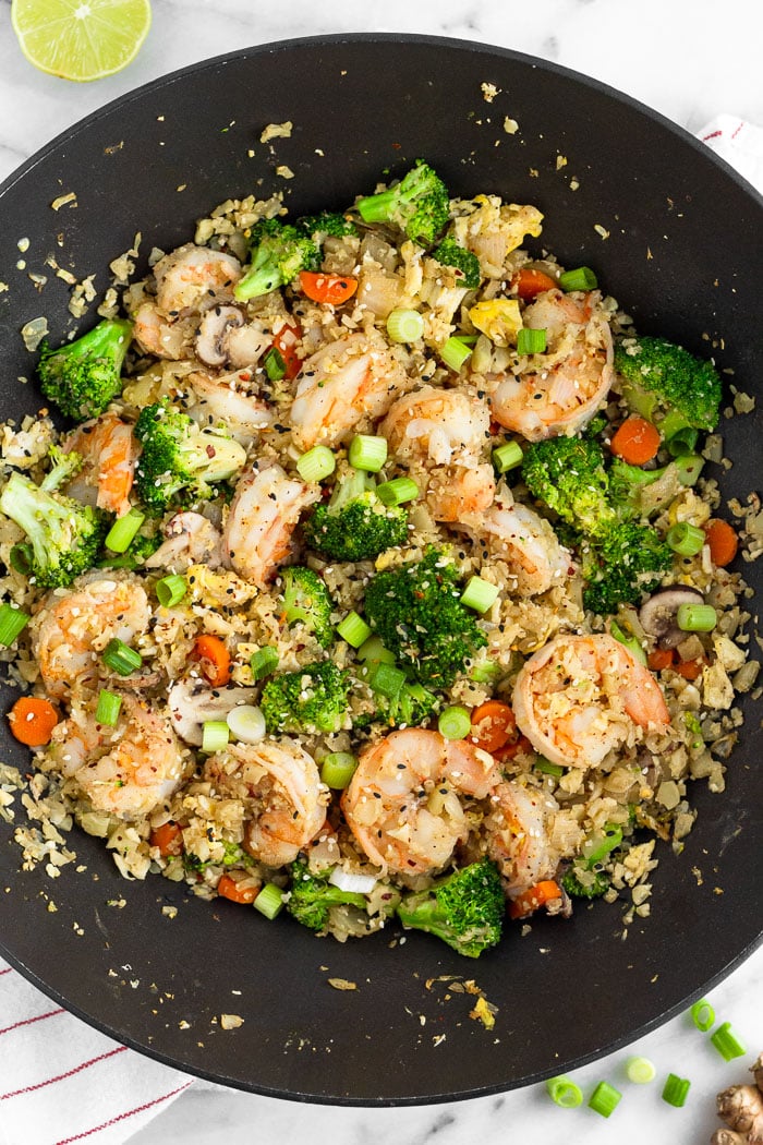 Large wok filled with cauliflower shrimp fried rice topped with sliced green onions and sesame seeds.