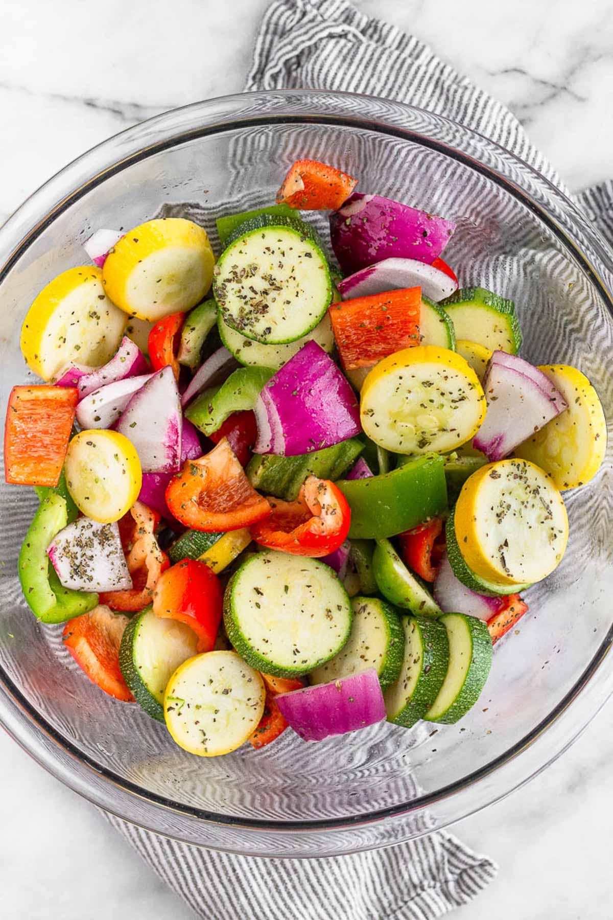 Large glass bowl with zucchini, pepper, and onion tossed with oil and spices.