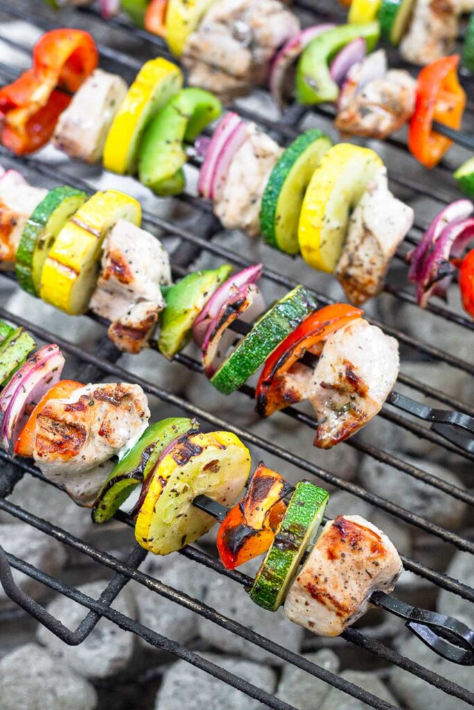 Chicken and veggie skewers being cooked on a grill.