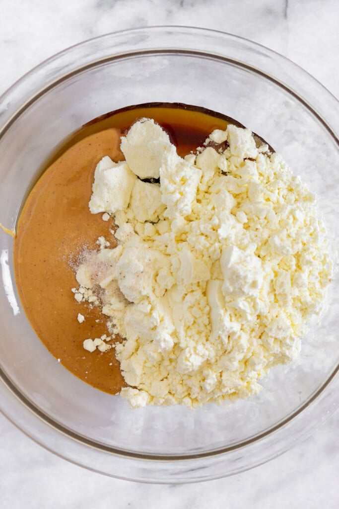 A glass bowl with peanut butter, maple syrup, protein powder, and salt before it is mixed together.