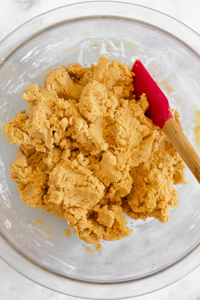 Peanut butter dough in a glass bowl with a spatula in it.