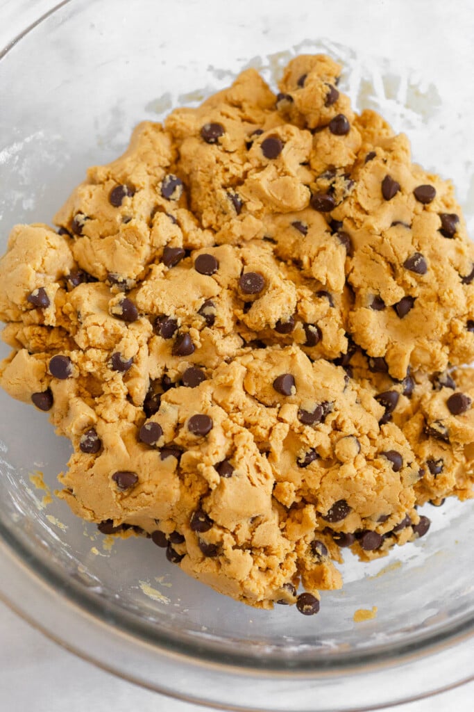 A glass bowl with peanut butter dough with chocolate chips mixed in.