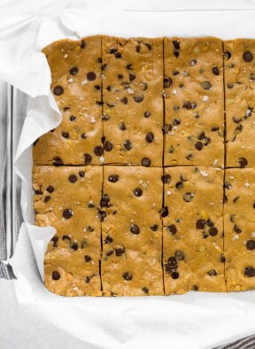 Glass pan lined with parchment paper filled with chocolate chip peanut butter perfect bar recipe.