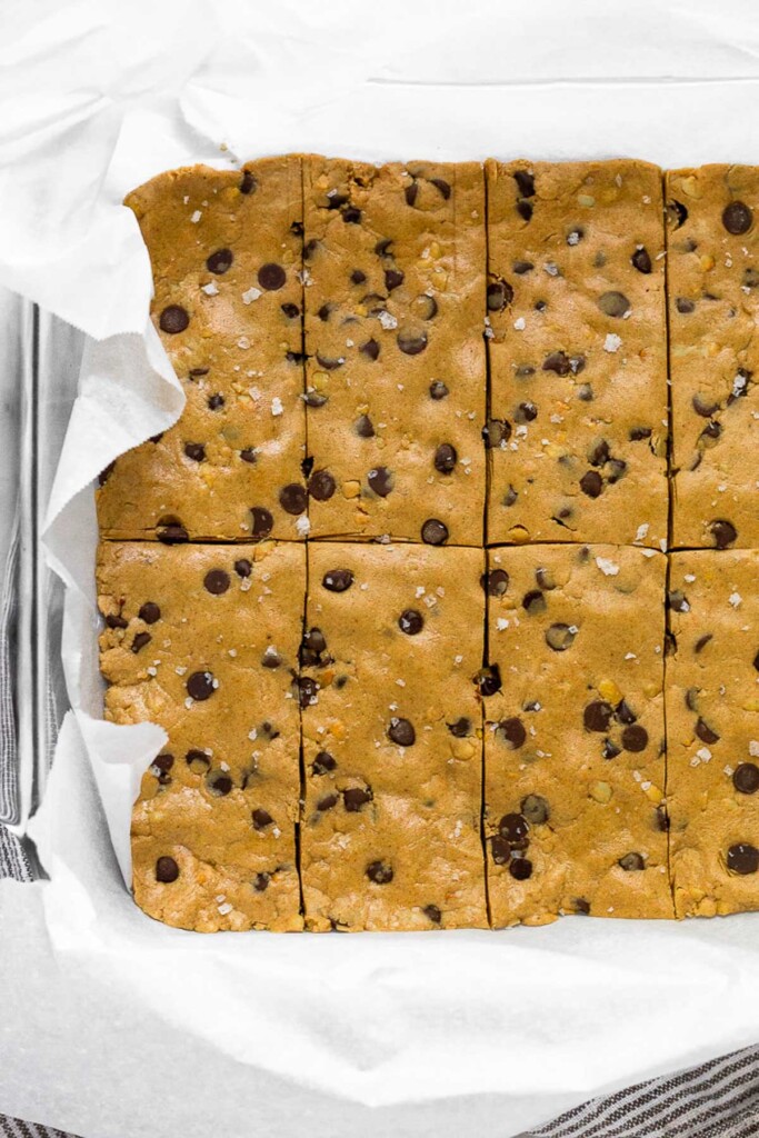 Glass pan lined with parchment paper filled with chocolate chip peanut butter perfect bar recipe.