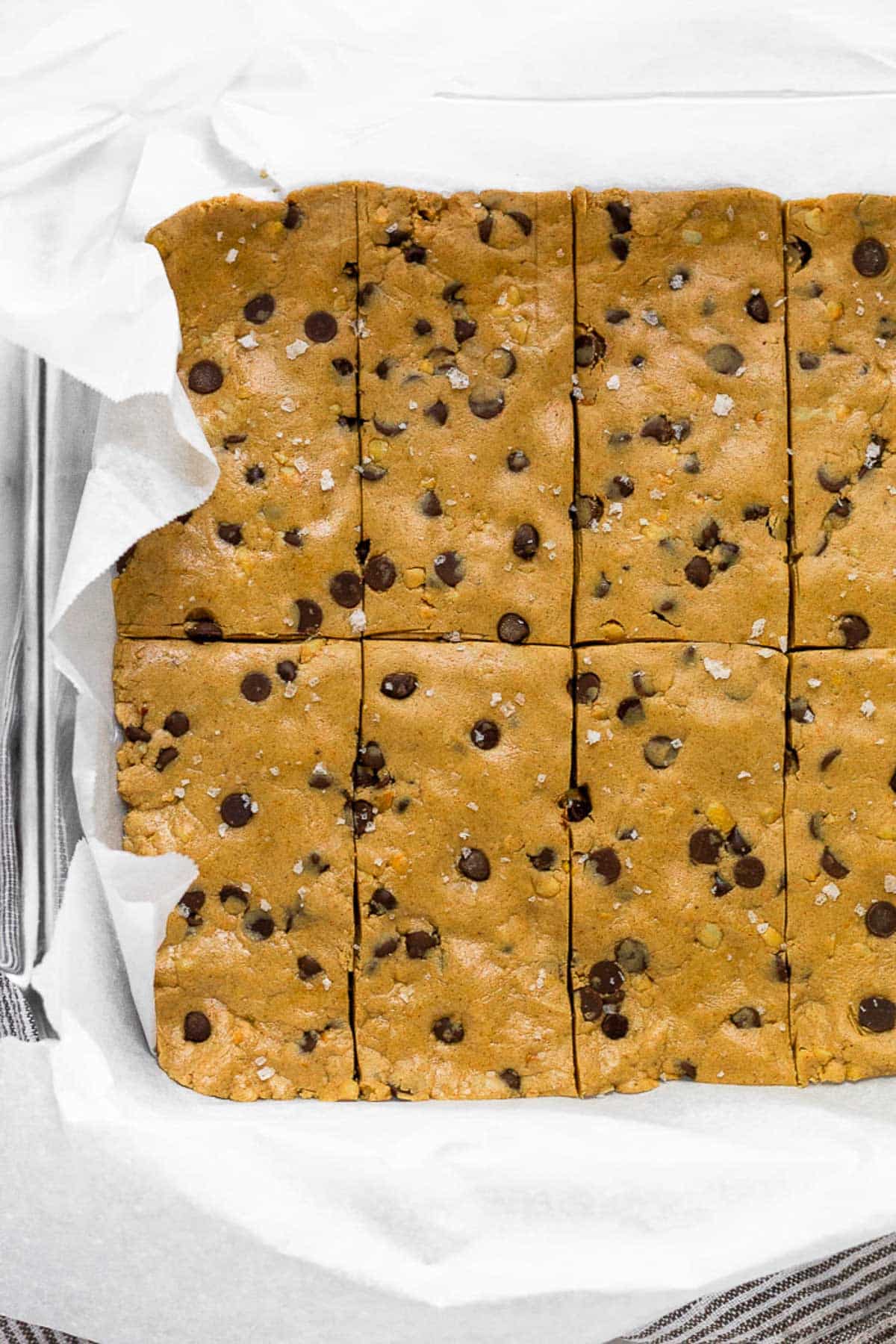 Glass pan lined with parchment paper filled with chocolate chip peanut butter perfect bar recipe.