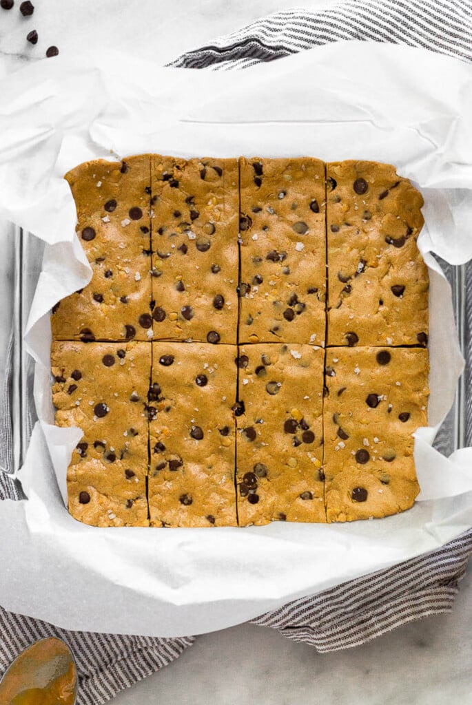 Glass baking dish lined with parchment paper filled with copycat perfect bar recipe.