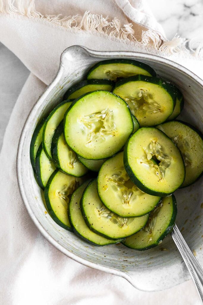 Bowl of marinated cucumbers with a spoon sticking out of it.