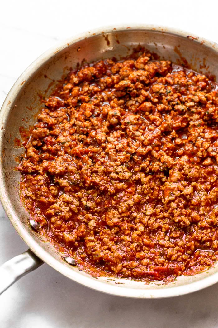 A large saute pan filled with sautéed ground pork, pizza sauce, and spices,