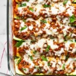 Healthy zucchini pizza boats in a large glass dish toped with fresh basil and red pepper flakes. The pan is sitting on a stripped towel with basil leaves next to it.