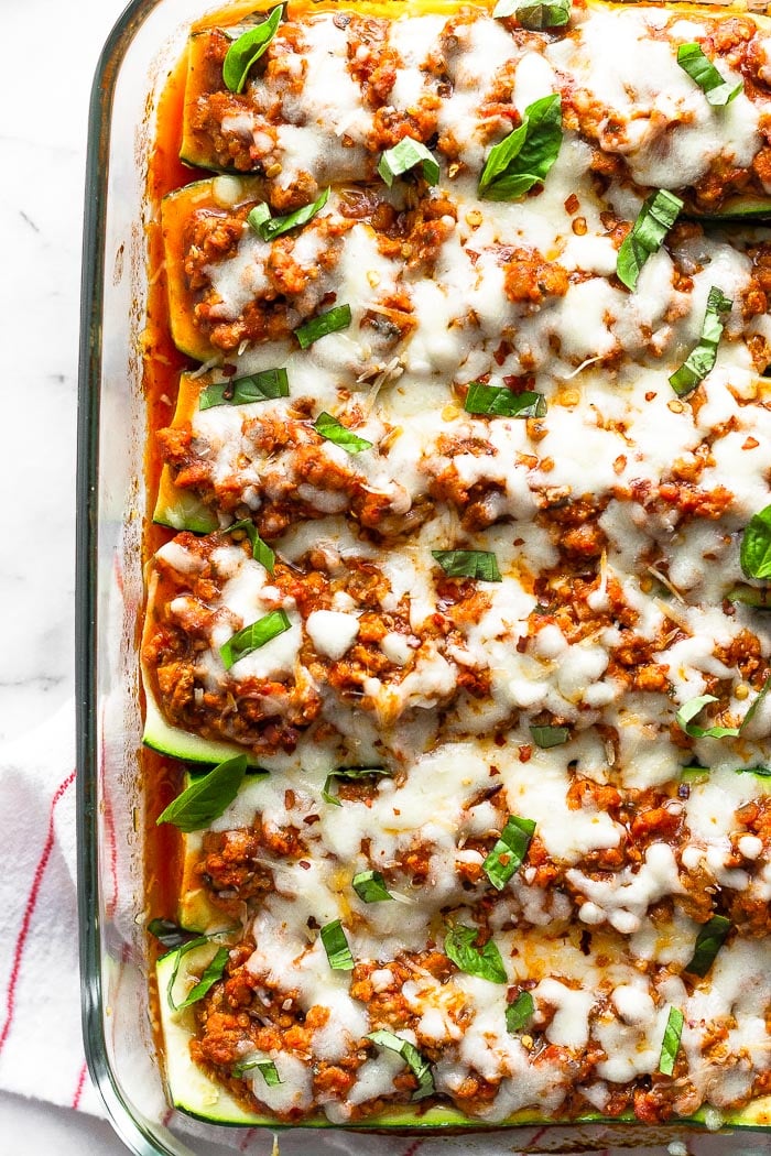 Overhead view of zucchini pizza boats topped with fresh basil in a glass baking dish.